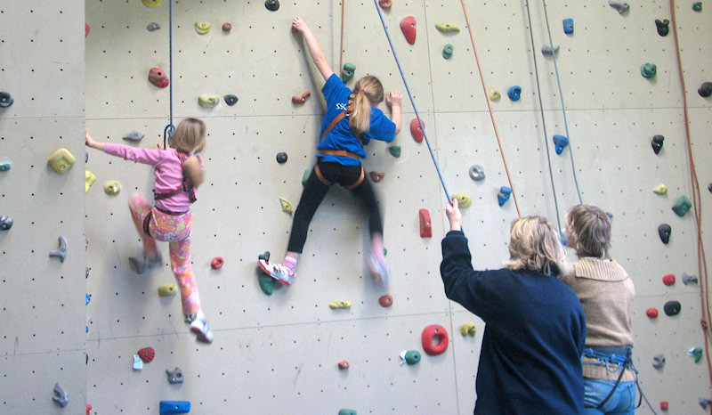 Eltern helfen ihren zwei Töchtern bleim Klettern auf einer Kletterwand.