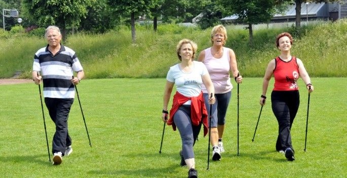 Drei ältere Frauen und ein Mann machen Nordic Walking.