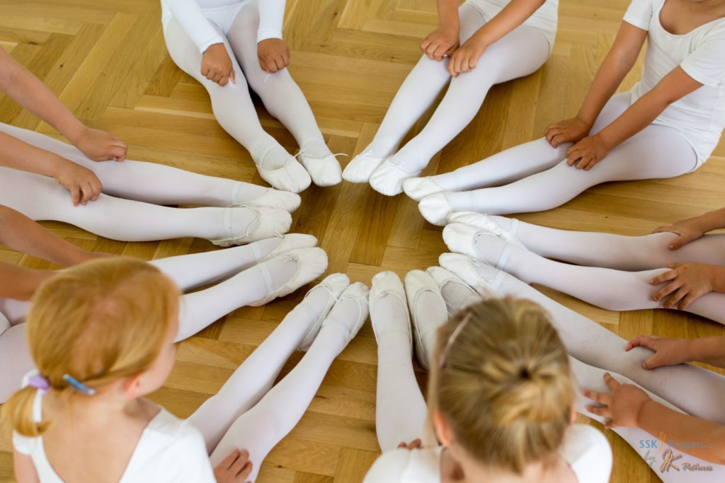 Junge Ballerina-Tänzerinnen sitzen im Kreis und bilden einen Kreis mit ihren Füßen.